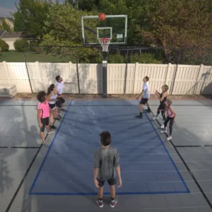 Seven people grouped around a Sport Court basketball hoop