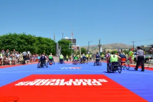 Wheelchair basketball game at an outdoor event with red and blue Sport Court flooring