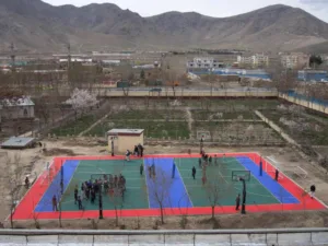 Groups of people on an outdoor game court surrounded by buildings and mountains