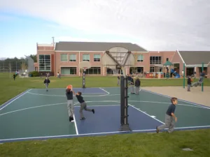 Young students playing outside on swings, playground equipment, and a basketball court