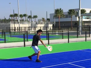 A boy playing pickleball on an outdoor court with palm trees in the background