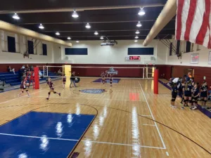 Girls' volleyball game in a school gymnasium with a volleyball net