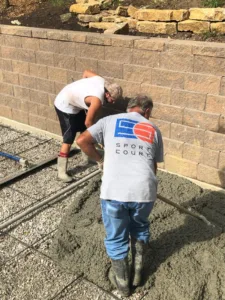 Two Sport Court installation crew members spreading a concrete base for a outdoor court