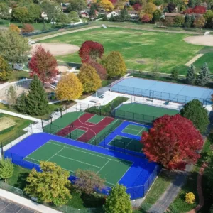 Overhead view of a multi-sport complex showcasing basketball and tennis courts with blue and green surfaces during autumn