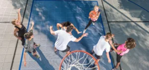 "Group of adults and kids, totaling seven people, playing basketball on an outdoor court surface"