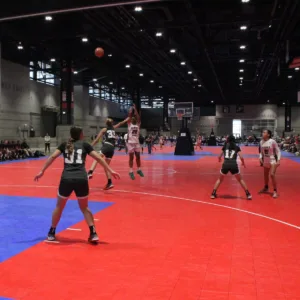 Girls playing a competitive indoor basketball game on red and blue court flooring