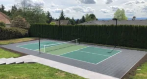 An outdoor residential pickleball court in a backyard lined with arborvitae trees