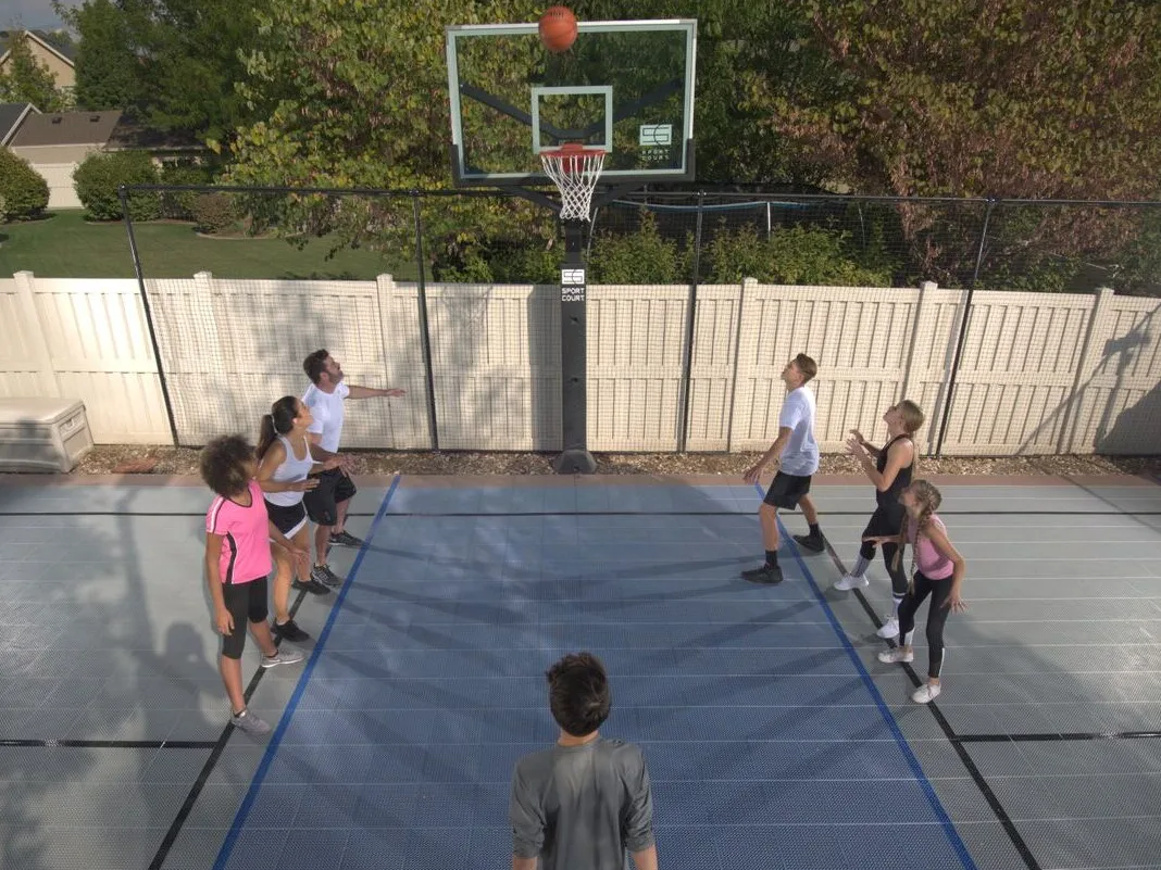 Seven people grouped around a Sport Court basketball hoop